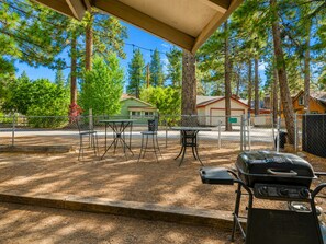 An outdoor patio area with a barbecue grill, a table with chairs, and a covered seating area.