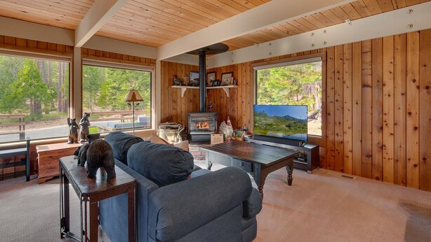 A cozy cabin interior with a fireplace, comfortable seating, and large windows offering scenic views. - Cozy Wood Cabin By Tahoe Getaways - 3 BR w Hot Tub, Fireplace + Backs to Forest (Carnelian Bay)