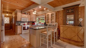 A spacious kitchen with wooden cabinets, a central island, and a bar area. - Cozy Wood Cabin By Tahoe Getaways - 3 BR w Hot Tub, Fireplace + Backs to Forest (Carnelian Bay)