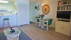 Un salon avec une table basse en verre, une table à manger avec des chaises, une bibliothèque, un téléviseur et un ventilateur de plafond.