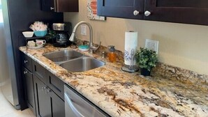 Una cocina con armarios oscuros, encimera de granito, un lavabo, una cafetera y un rollo de servilletas de papel.