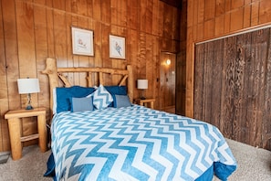 A wooden-paneled bedroom with a bed, two nightstands, and a large mirror.