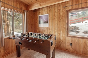 A wooden-floored room with a foosball table, large windows, and a framed picture on the wall.