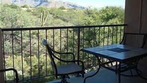 Ein Balkon mit Tisch und Stühlen, mit Blick auf eine gebirgige Landschaft.