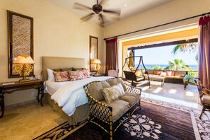 A hotel room with a bed, a sofa, a ceiling fan, and a view of the ocean. - Resort Living in Ocean View Penthouse at Esperanza (Cabo San Lucas)