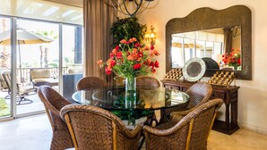 A dining area with wicker chairs, a glass table, a vase with red flowers, a chandelier, and a large mirror. - Resort Living in Ocean View Penthouse at Esperanza (Cabo San Lucas)