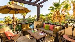 A patio area with outdoor furniture, including a sofa and chairs, a table with a drink and glasses, and a large umbrella providing shade. - Resort Living in Ocean View Penthouse at Esperanza (Cabo San Lucas)