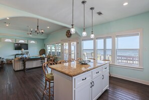 A spacious kitchen with a large island, wooden flooring, and a view of the ocean through large windows.