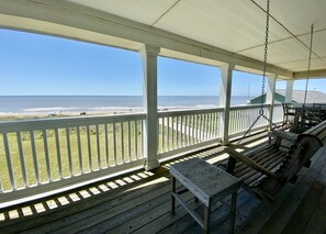 Een houten veranda met uitzicht op de oceaan, een schommel en een tafel.