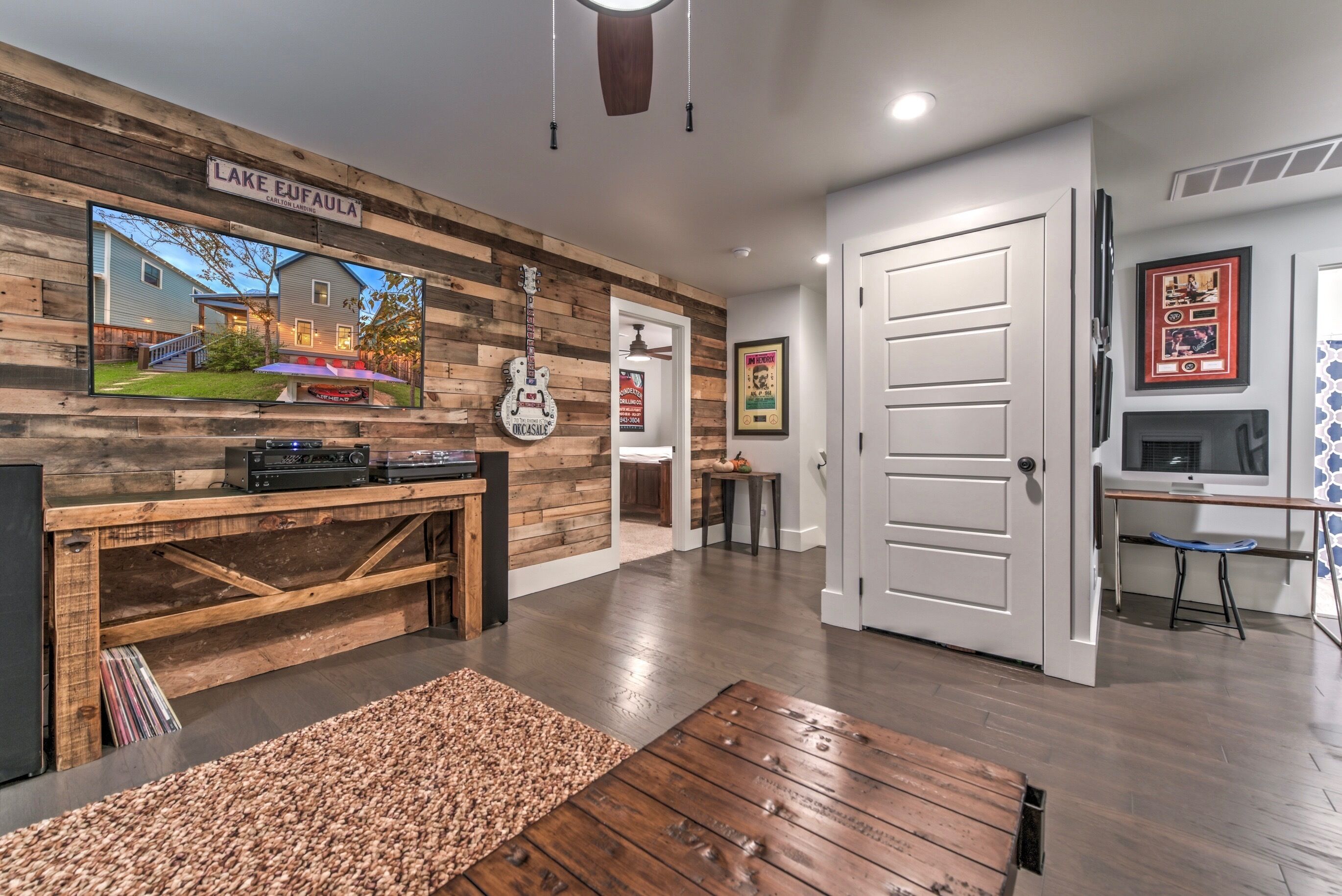 A modern living room with a wooden wall, a mounted TV, a guitar, and a door leading to another room.