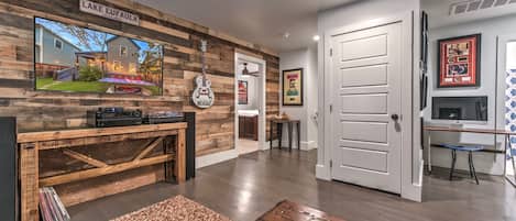 A modern living room with a wooden wall, a mounted TV, a guitar, and a door leading to another room.