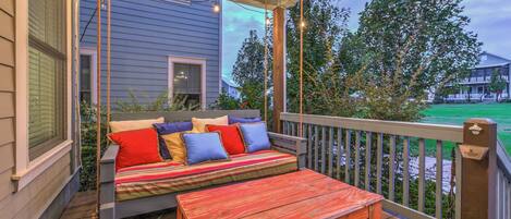 A wooden deck with a swing seat and a bench, overlooking a green landscape.