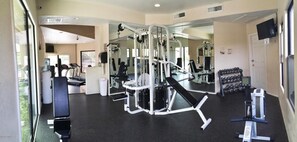 A gym with exercise equipment, mirrors, and a row of dumbbells.