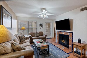 A living room with a sofa, coffee table, fireplace, TV, and ceiling fan.