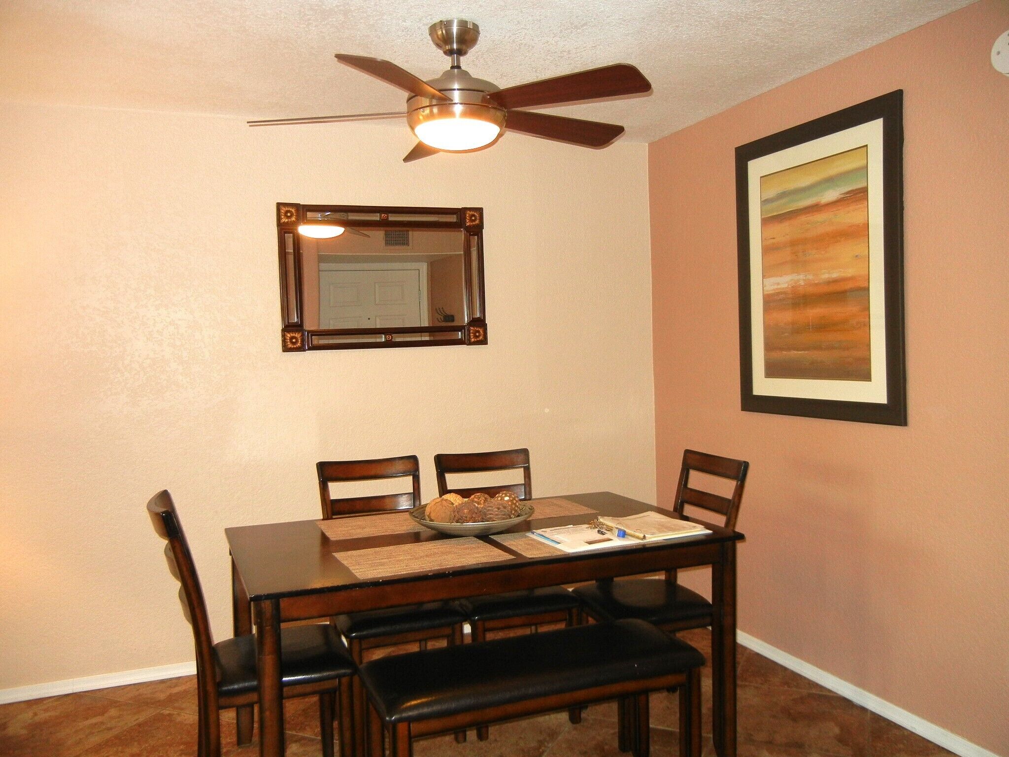 A dining area with a table, chairs, a ceiling fan, a mirror, and a framed picture on the wall.