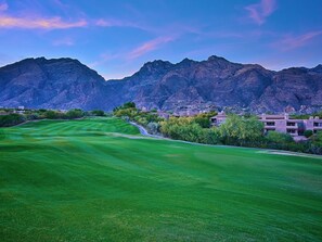 Un campo de golf con montañas al fondo, rodeado de edificios residenciales.
