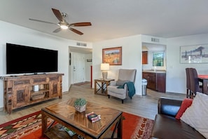 A living room with a television, wooden entertainment unit, a coffee table, a sofa, a chair, a lamp, and artwork on the walls. - Highly desired Eastside 1st floor - expanded patio and great Mountain Views! (Tucson)