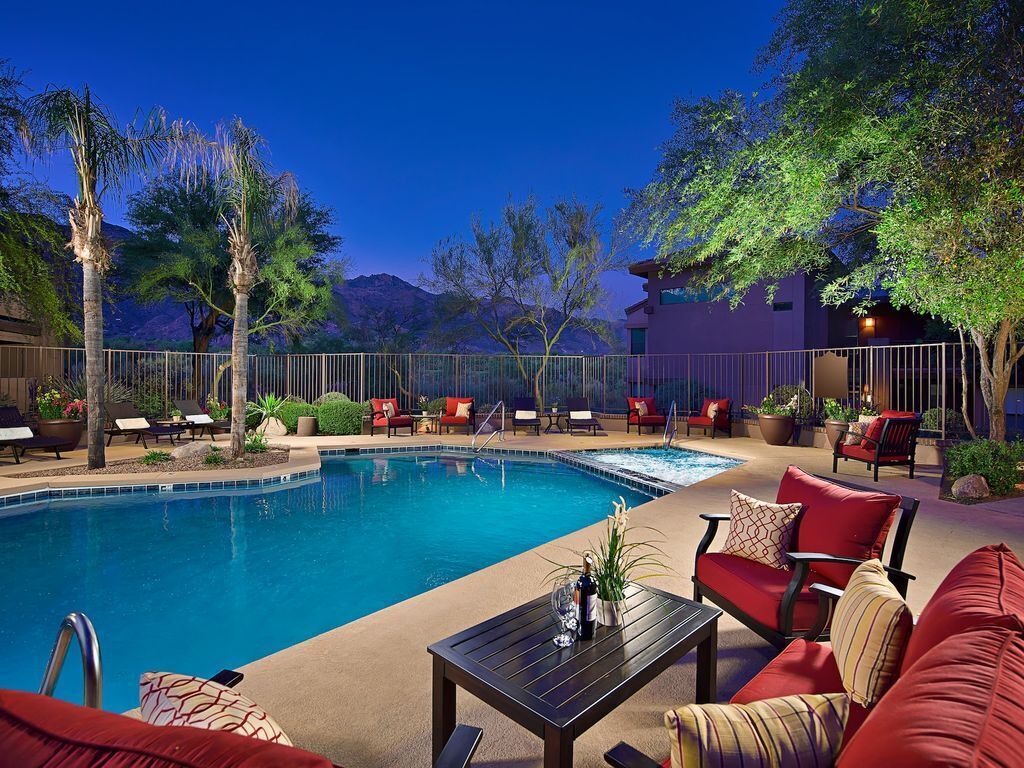 A poolside area with a pool, lounge chairs, and a seating area with red sofas and a table.