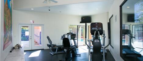 Een sportschool met trainingsapparatuur, een plafondventilator en een deur naar buiten.