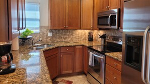 A modern kitchen with wooden cabinets, granite countertops, stainless steel appliances, and a window with blinds. - Stunning - Inside and out! Beautiful Inside and Views of the Catalinas! (Tucson)