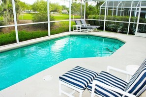 Piscina com espreguiçadeiras e uma estufa ao fundo.