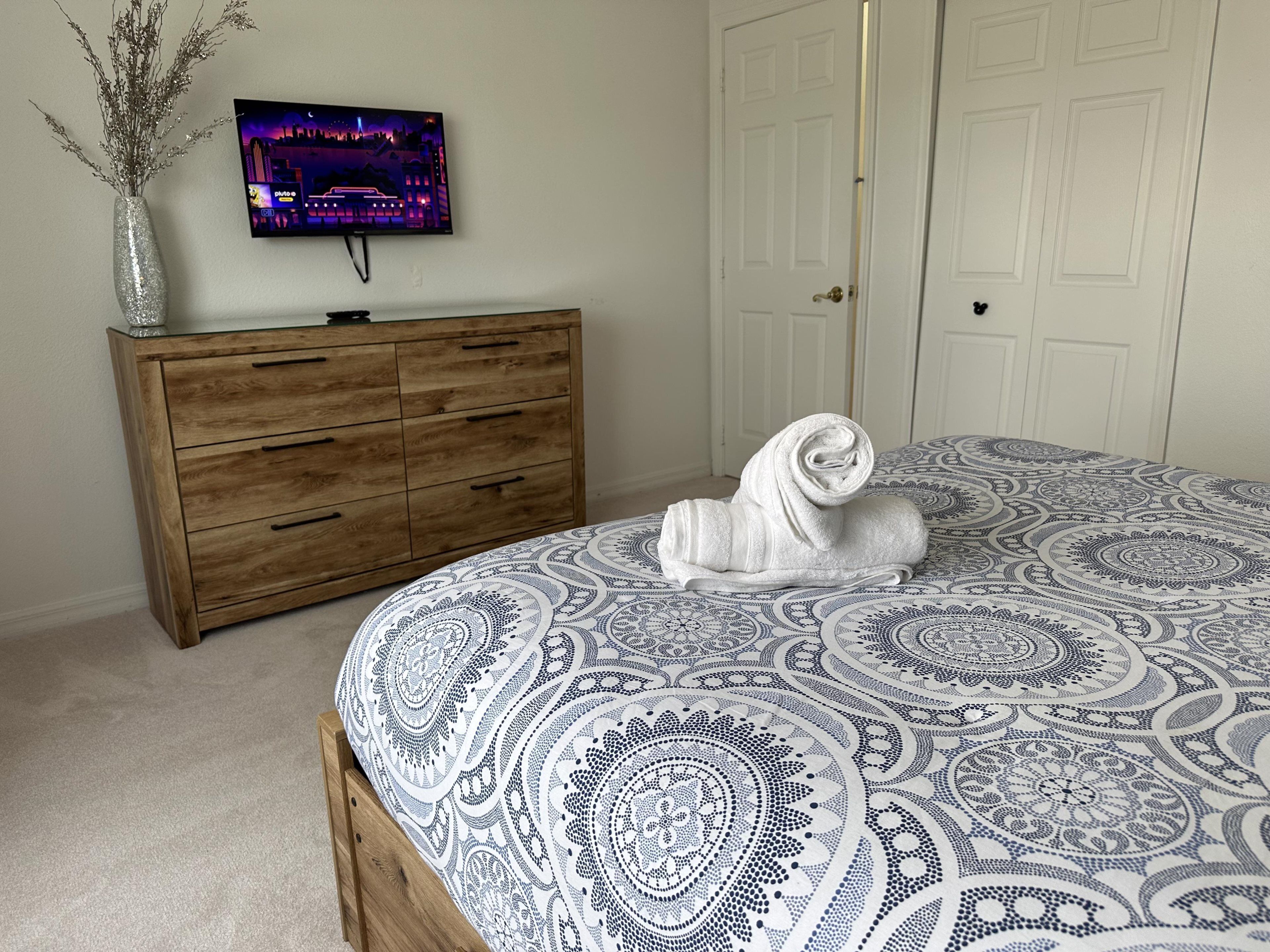 Un dormitorio con una cama, un aparador de madera, un televisor en la pared y una puerta.