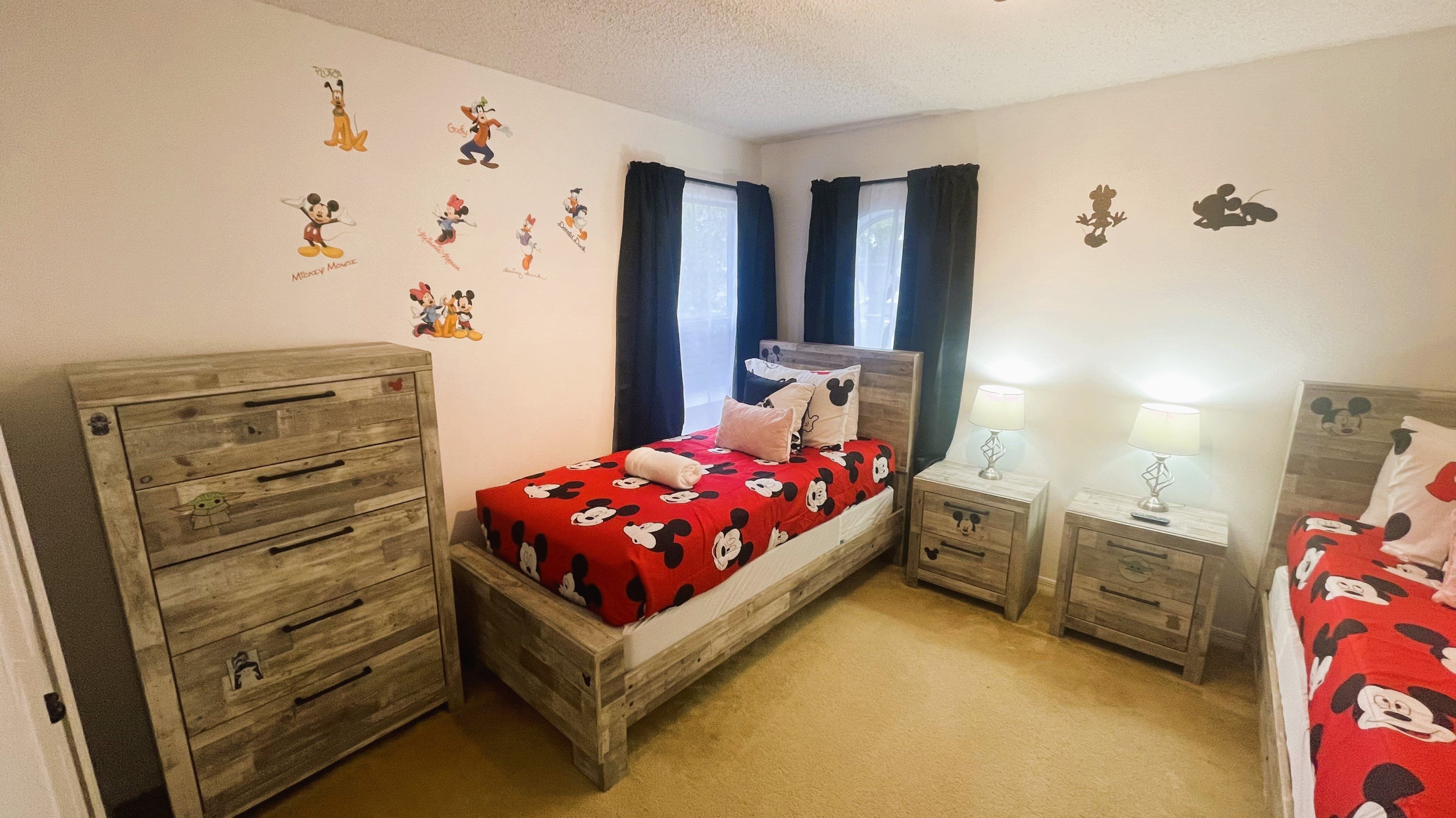 Ein Schlafzimmer mit einem hölzernen Bett, zwei Nachttischen, einer Kommode und Mickey-Mouse-Dekoration.