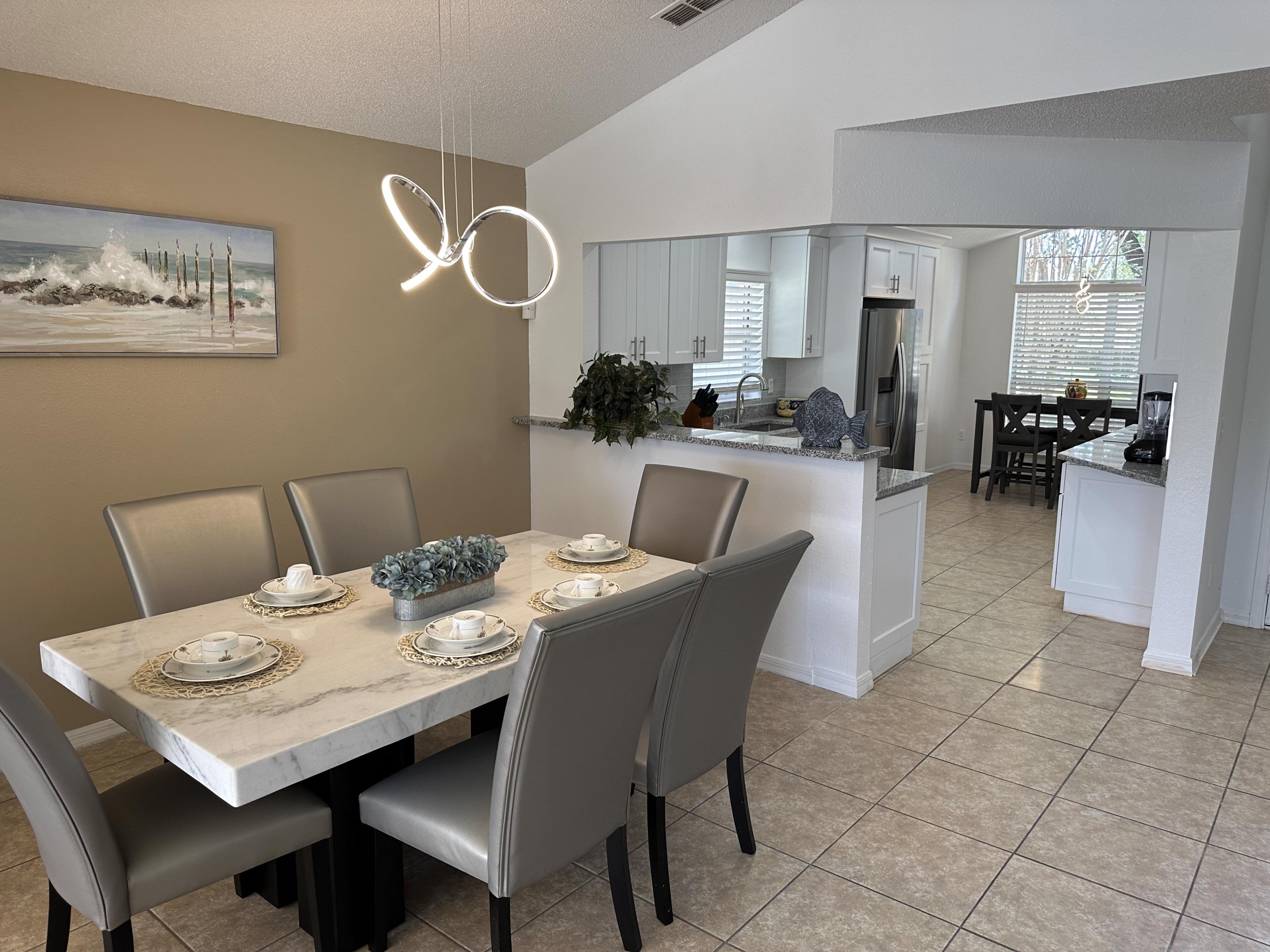 A modern kitchen with white cabinets, a built-in island, and a dining area with a marble table and grey chairs.