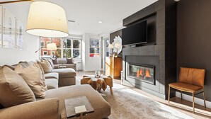 Ein modernes Wohnzimmer mit einer Couch, einem Couchtisch, einem Kamin und einem an der Wand befestigten Fernseher.