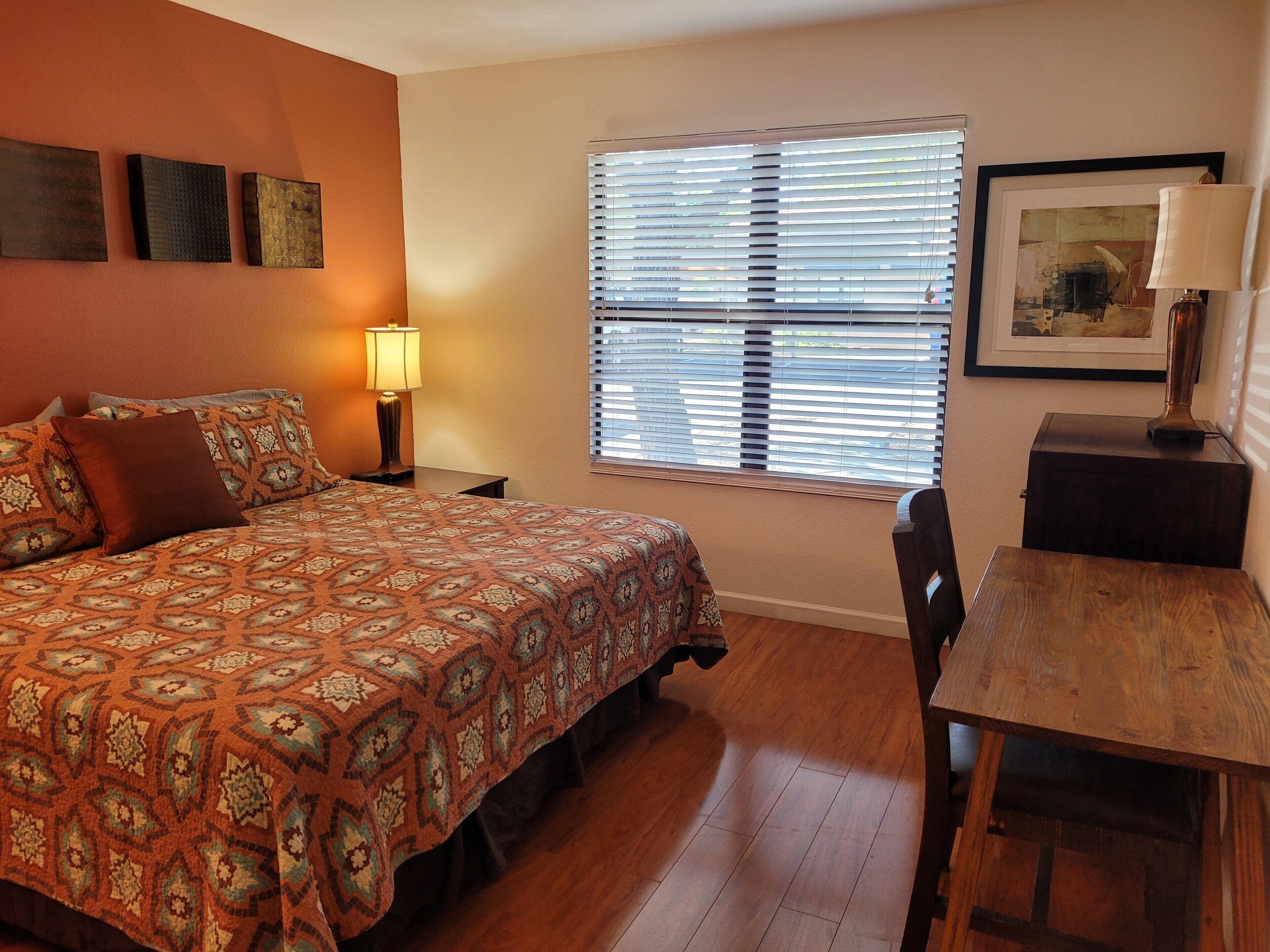 A bedroom with a bed, a desk, a chair, a lamp, and a window with blinds.