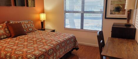 A bedroom with a bed, a desk, a chair, a lamp, and a window with blinds.