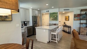 A modern kitchen with white cabinets, a central island with bar stools, and a dining area with a wooden table and chairs. - Best VIEWS & largest Extended Patio in the entire community of The Greens (Tucson)