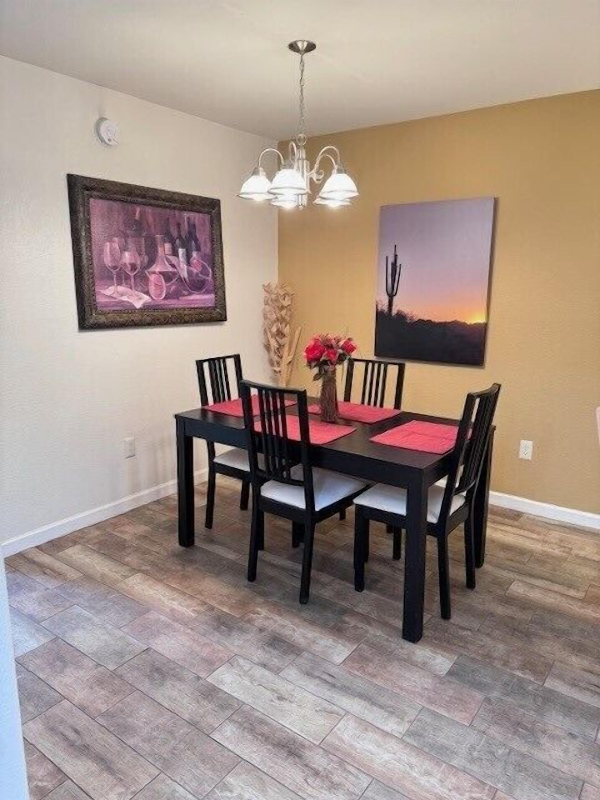 A dining area with a black table and chairs, a chandelier, and two framed artworks on the walls.