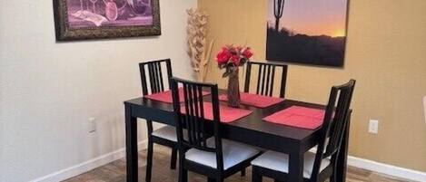 A dining area with a black table and chairs, a chandelier, and two framed artworks on the walls.
