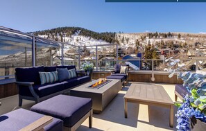 Relax in a serene outdoor space with a sofa, ottomans, and fire pit, surrounded by breathtaking mountain views.