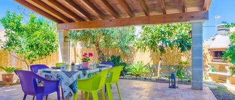 An outdoor patio with a wooden pergola, a table set for dining, and colorful chairs.