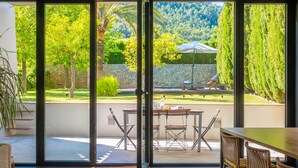 A modern room with a large sliding glass door leading to an outdoor patio. The patio features a dining table with chairs, a small umbrella, and a stone wall. - CAN CABRIT - Modern villa with private pool at the foot of the mountain. Free WiFi (Alaro)