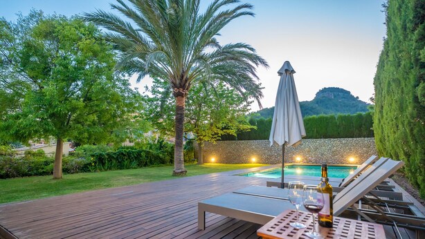 A wooden deck with lounge chairs and a table, a swimming pool, and a stone wall with lights. - CAN CABRIT - Modern villa with private pool at the foot of the mountain. Free WiFi (Alaro)