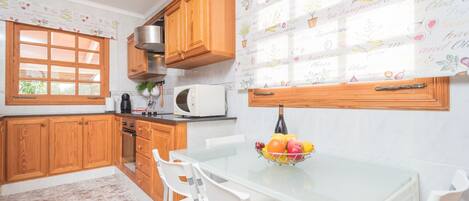 A kitchen with wooden cabinets, a microwave, a sink, and a dining table with chairs.
