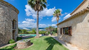 Une cour bordée de murs en pierre, avec un palmier, une piscine et une vue sur des montagnes lointaines.