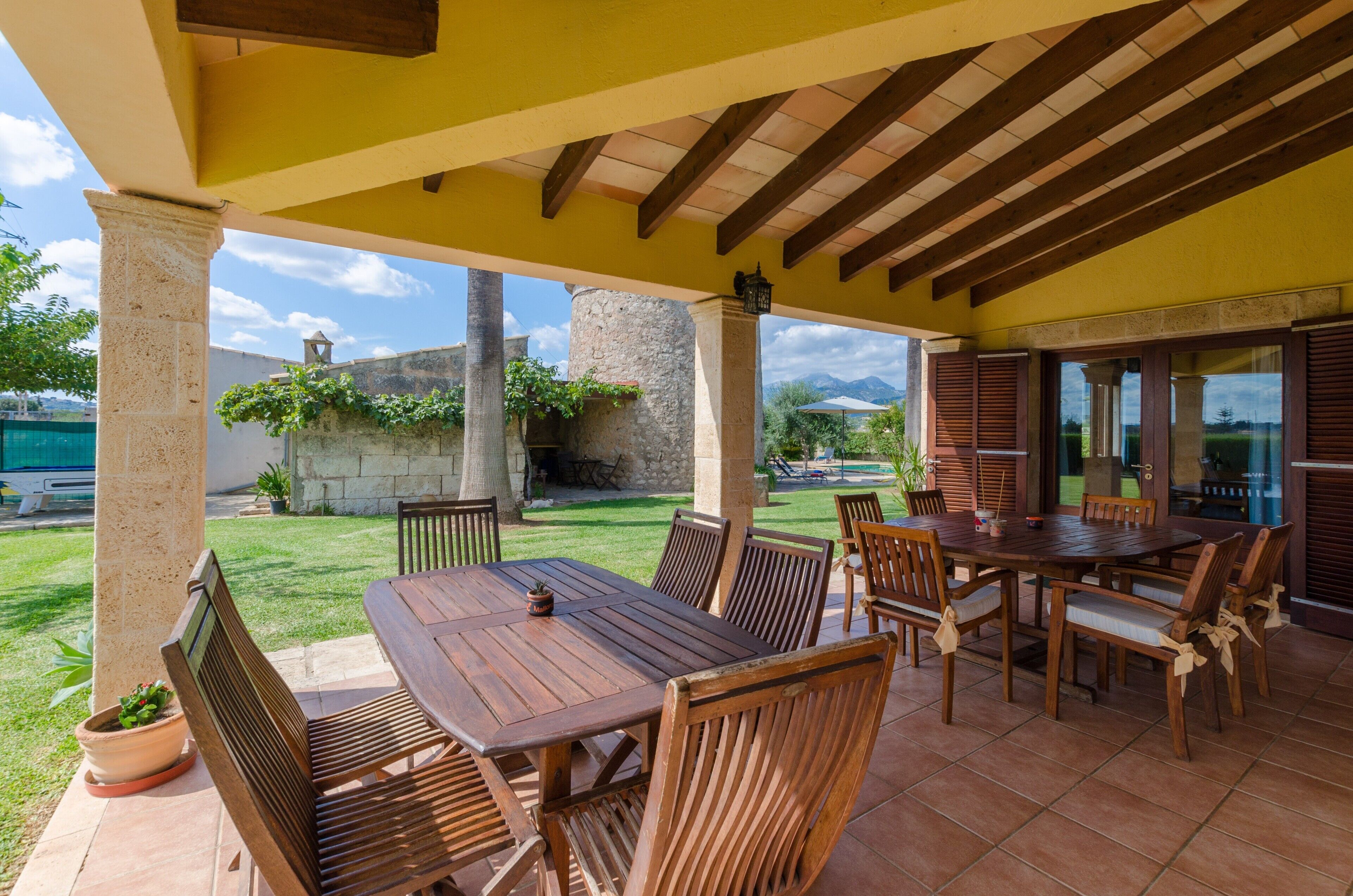 An outdoor patio with a wooden table and chairs, a stone pillar, and a view of a mountain in the background.