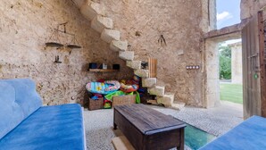 Une pièce rustique aux murs de pierre, avec une table en bois, un canapé bleu et un escalier menant à un espace extérieur.