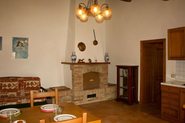 A dining area with a brick fireplace, wooden furniture, and a hanging light fixture. - Beautiful apartment for 4 guests with pool, WIFI, TV and pets allowed, close to Cortona (Castiglion Fiorentino)