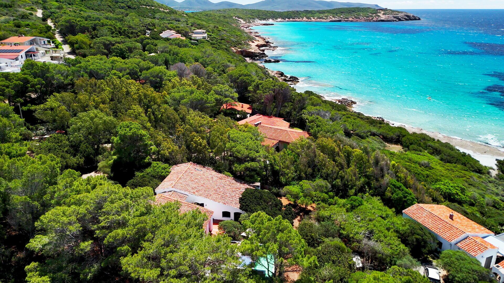 Um imóvel costeiro com vários edifícios rodeado por vegetação densa, com vista para um mar azul-turquesa.