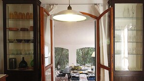 Un comedor con una mesa dispuesta para cuatro personas, vistas al exterior y un amplio ventanal con cortinas.