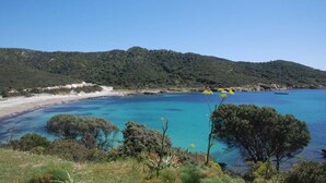 Un paisaje costero con mar azul cristalino, colinas verdes y una playa.