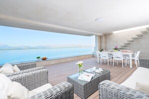 A modern outdoor seating area with wicker furniture, a dining table, and a view of a body of water. - AIXA - Chalet with sea views in Es Barcarés - Alcúdia . Free WiFi (Alcúdia)