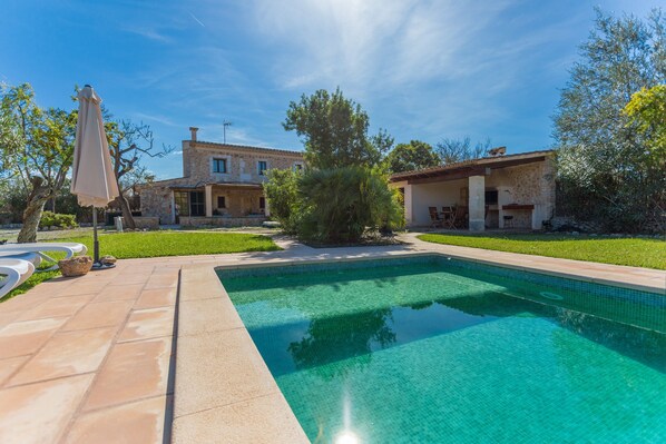 A rectangular swimming pool with clear blue water, surrounded by a paved patio area.