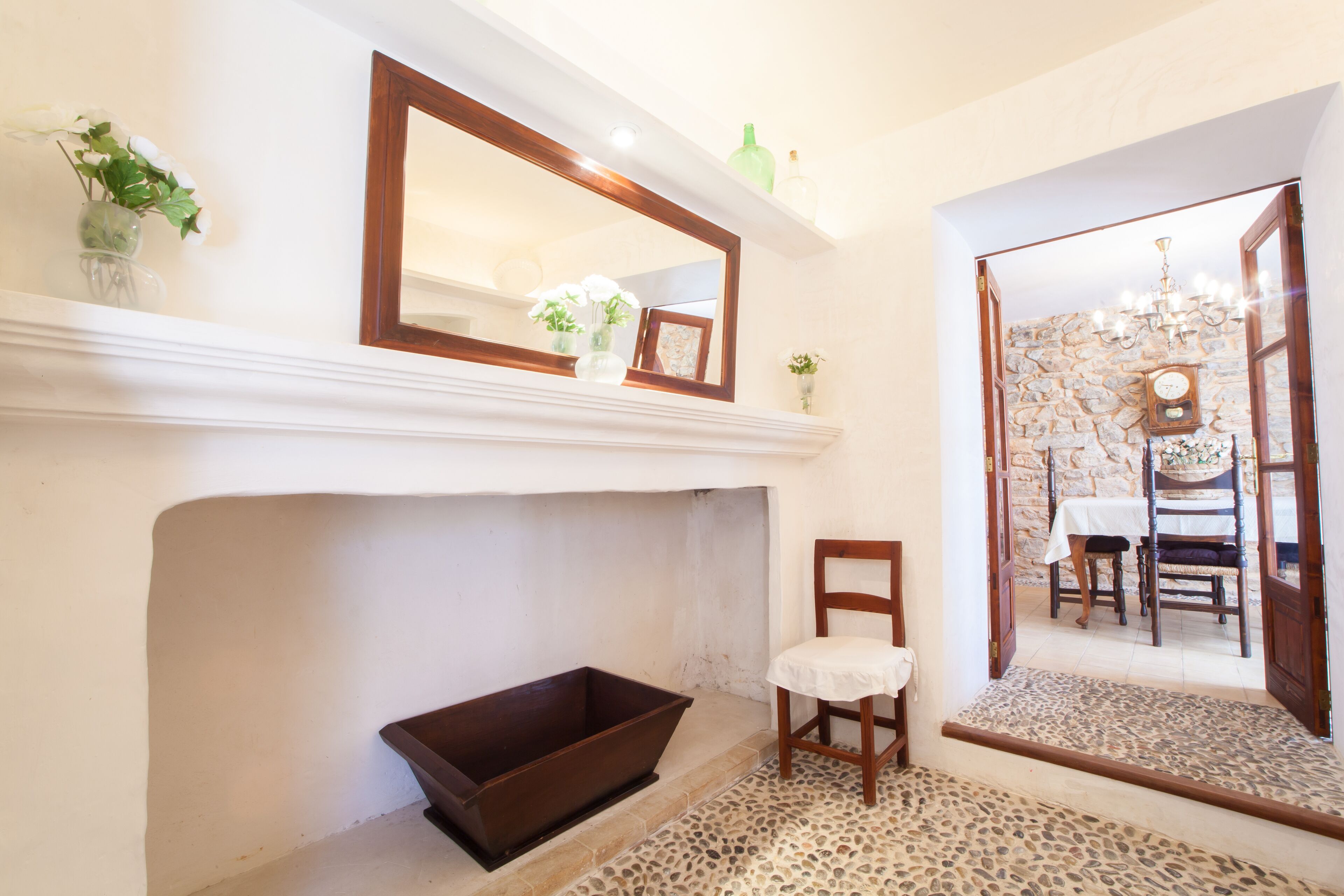 A room with a fireplace, a mirror, a chair, and a view of a dining area through an open door.