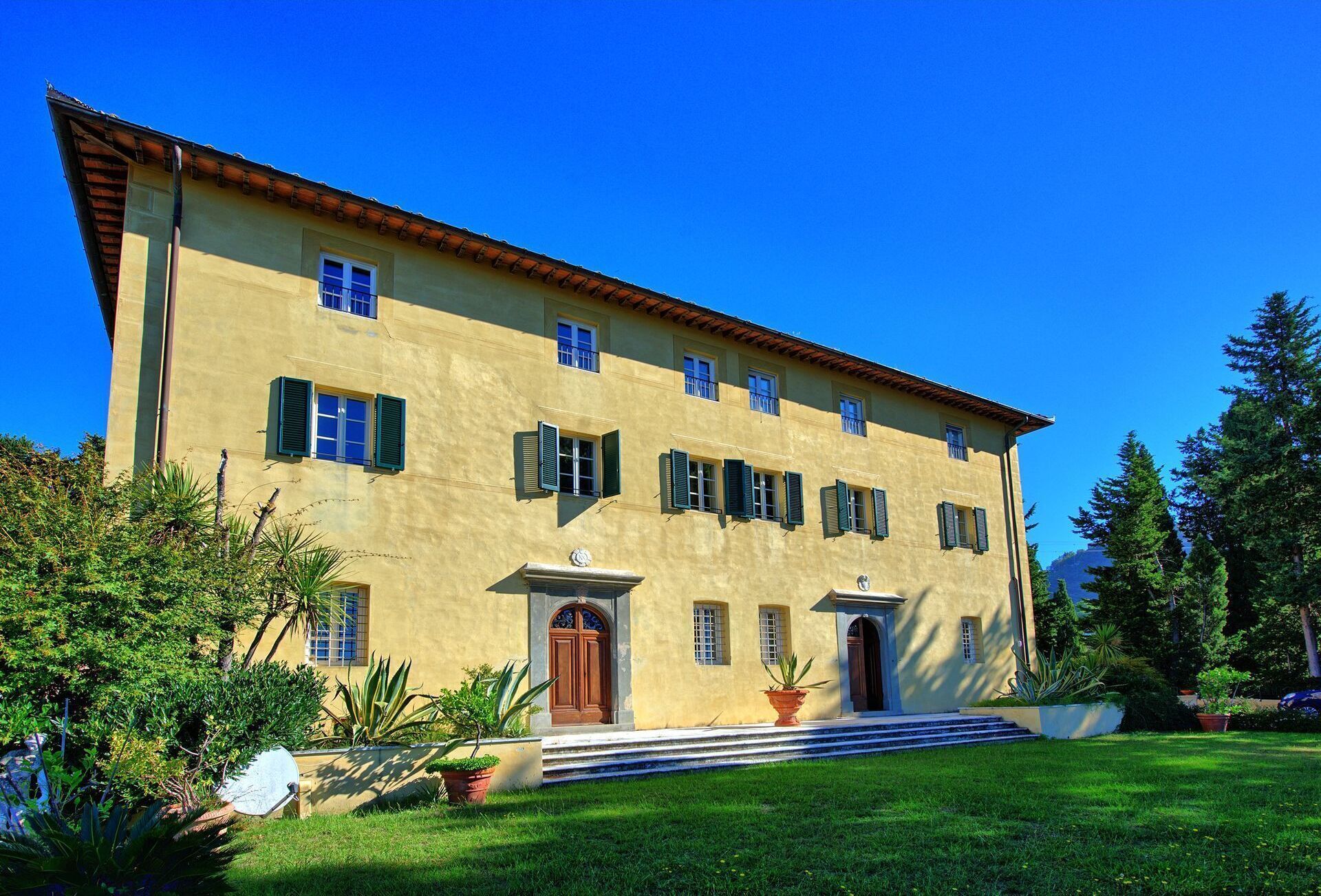 A two-story building with a yellow facade, multiple windows with shutters, and a central entrance with a door.